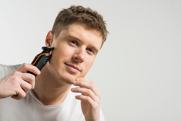 Smiling young man shaving with machine isolated on white background