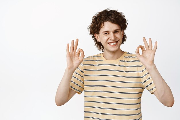 Smiling young man showing okay zero gesture say no problem approve something standing over white background