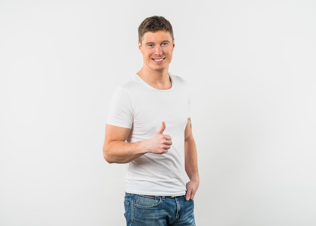 Smiling young man showing thumb up sign against white background