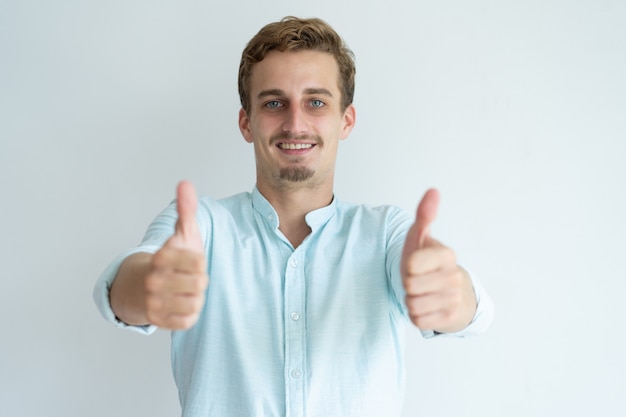 Smiling young man showing thumbs up and looking at camera. 