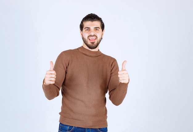 smiling young man showing thumbs up on white wall. 