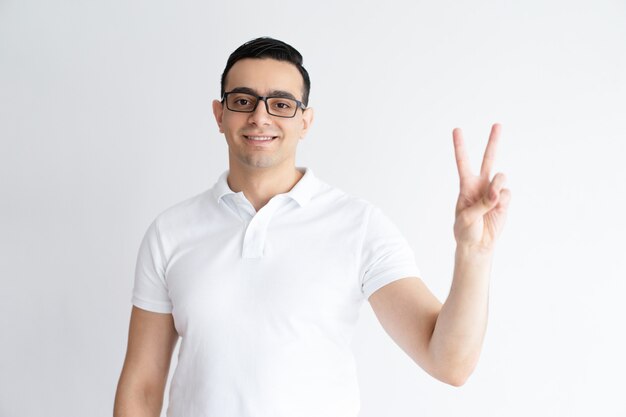 Smiling young man showing victory sign and looking at camera.