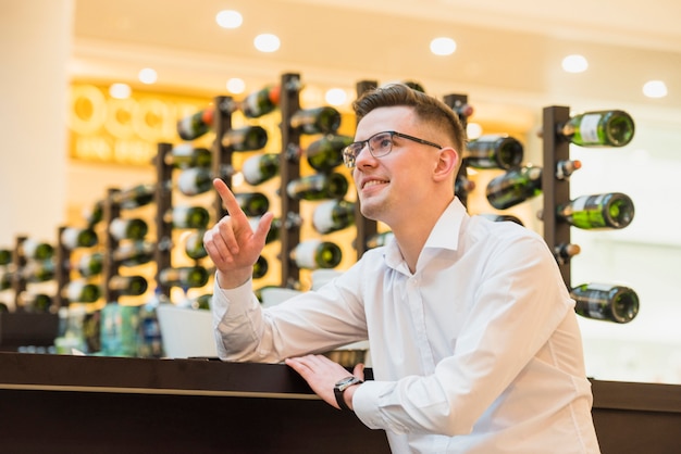 Smiling young man sitting near the bar counter pointing his finger