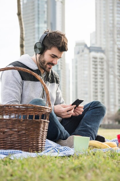 公園に座っている若い男を笑って、携帯電話で音楽を聴いている