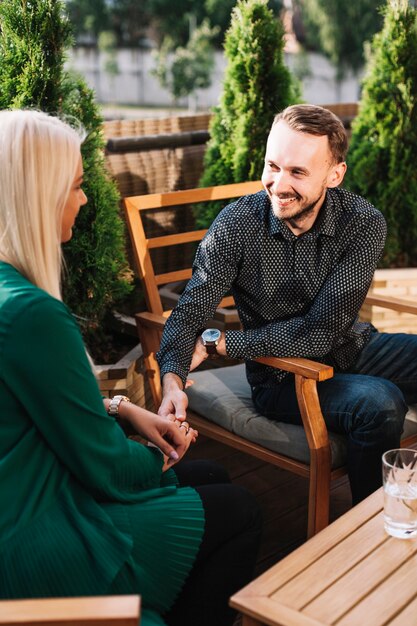 Smiling young man sitting in restaurant holding blonde young woman's hand