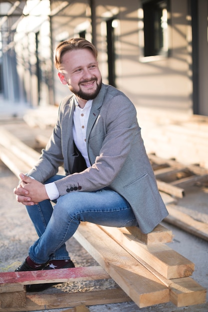 Smiling young man sitting on wooden plank at outdoors