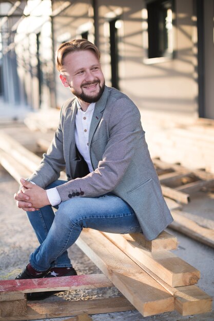 Smiling young man sitting on wooden plank at outdoors