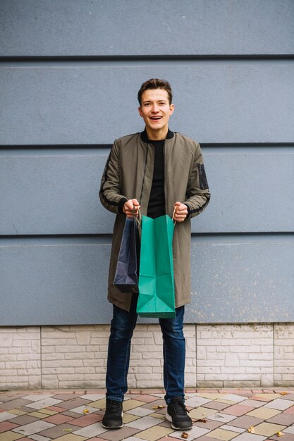 Smiling young man standing against wall holding shopping bags