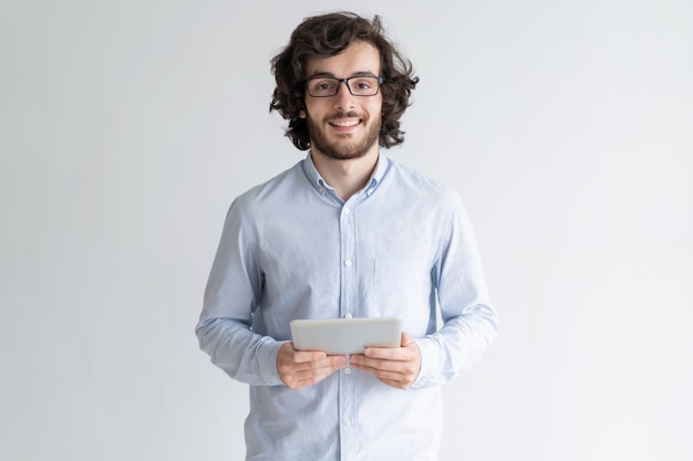 Smiling young man standing and holding tablet computer