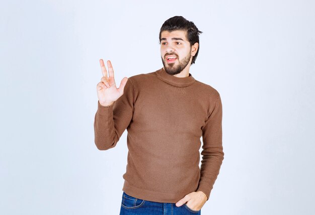 smiling young man standing and showing victory sign .