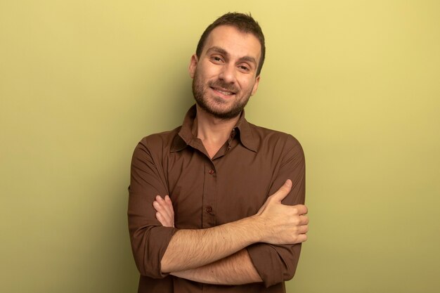 Smiling young man standing with closed posture looking at front isolated on olive green wall