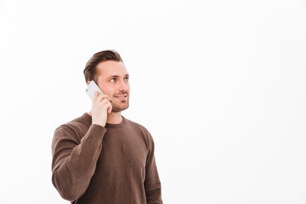 Smiling young man talking by mobile phone. Looking aside.