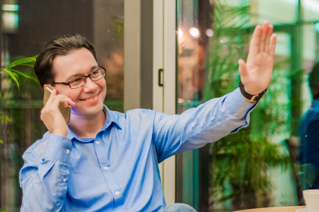 Smiling young man talking on the phone and showing greeting gesture