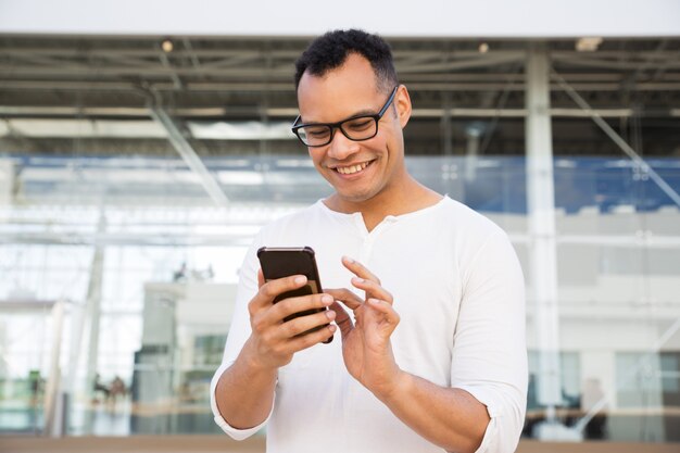 Улыбающийся молодой человек текстовых сообщений на смартфоне на открытом воздухе