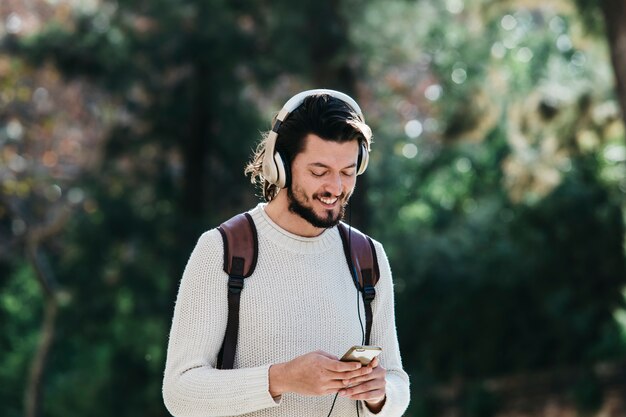 Smiling young man using phone for listening to music on headphone in the park