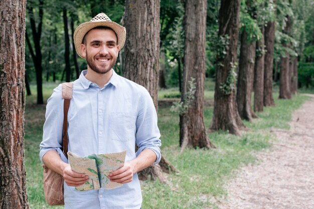 公園で地図を持って帽子をかぶっている若い男の笑みを浮かべてください。
