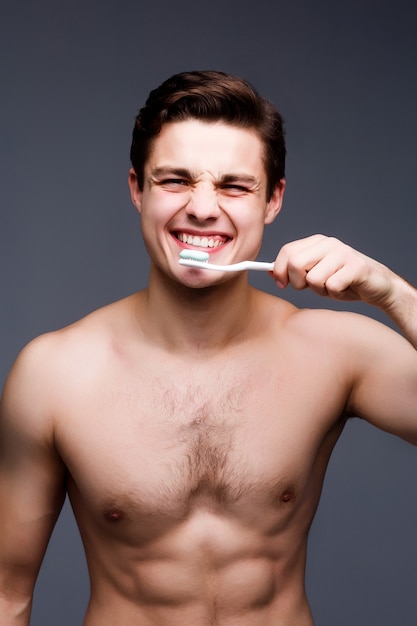 Smiling young man with toothbrush cleaning teeth isolated on black wall