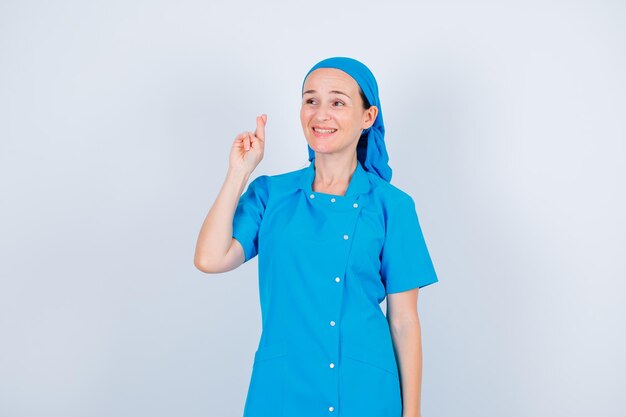 笑顔の若い看護師は目をそらし、白い背景に指を交差させています