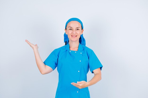 Smiling young nurse is pointing left with hand on white background