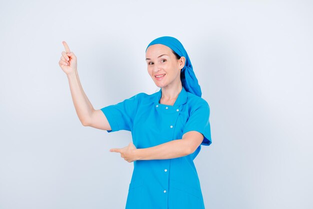 笑顔の若い看護師は白い背景の上の人差し指で上向きです