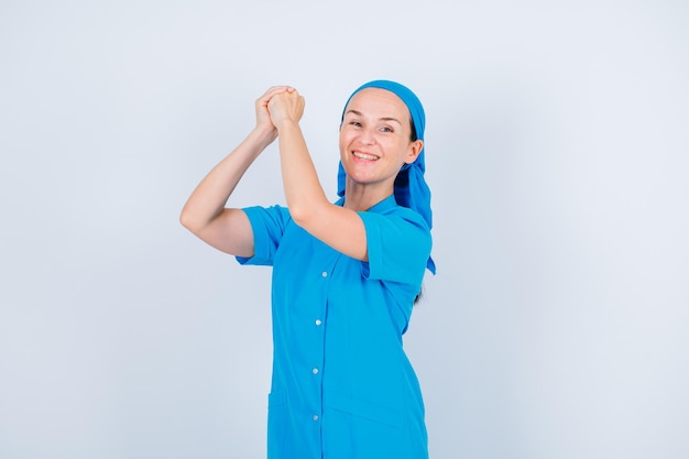 Улыбающаяся молодая медсестра поднимает и держит руки на белом фоне