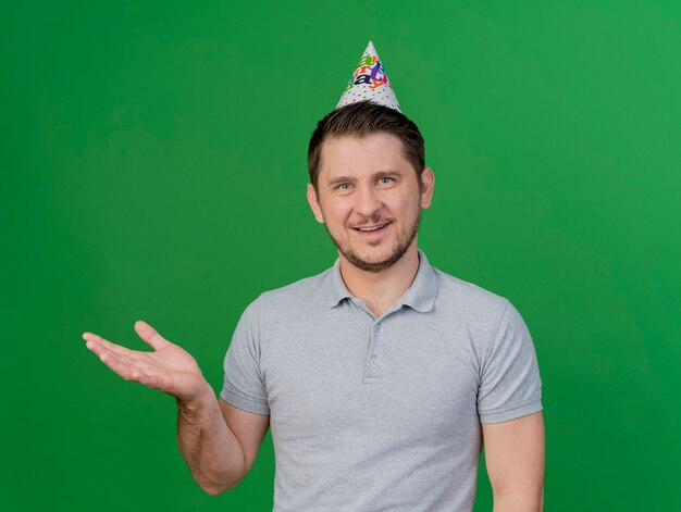 녹색에 고립 된 측면에서 손으로 생일 모자 포인트를 입고 웃는 젊은 파티 남자