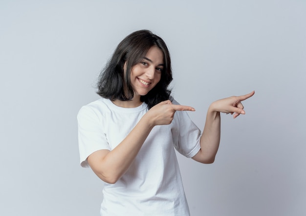 Smiling young pretty caucasian girl looking at camera and pointing at side isolated on white background