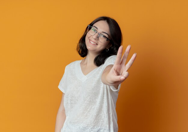 Smiling young pretty caucasian girl wearing glasses stretching out hand and showing three with it isolated on orange background with copy space