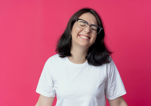 Smiling young pretty caucasian girl wearing glasses with closed eyes isolated on crimson background