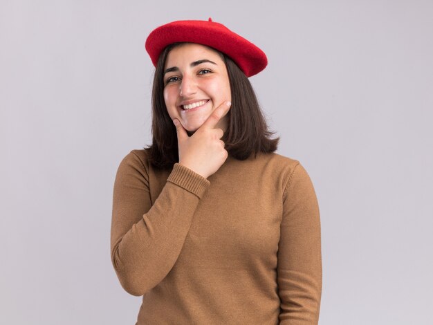 Smiling young pretty caucasian girl with beret hat holding chin on white