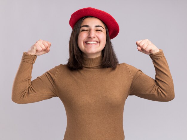 Smiling young pretty caucasian girl with beret hat keeping fists isolated on white wall with copy space