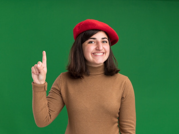 Smiling young pretty caucasian girl with beret hat points up