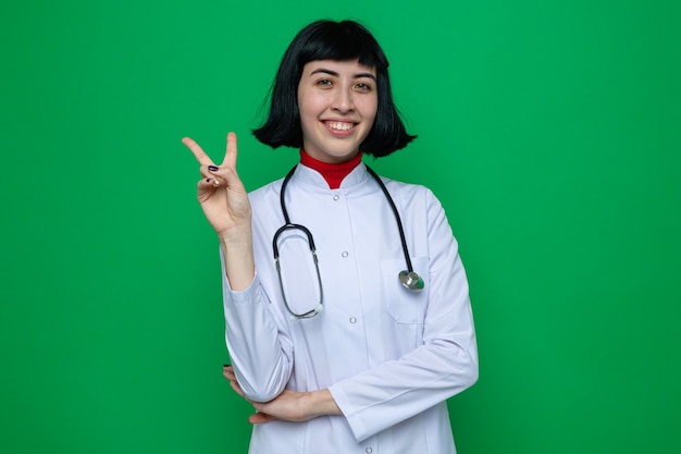 청진 기 승리 기호 몸짓으로 의사 유니폼에 웃는 젊은 예쁜 백인 여자