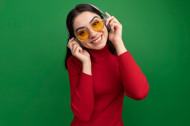 Smiling young pretty caucasian woman wearing sunglasses and headphones grabbing headphones