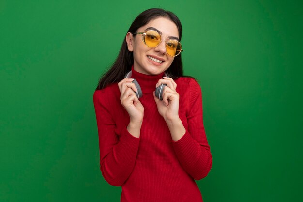 Smiling young pretty caucasian woman wearing sunglasses and headphones on neck grabbing headphones