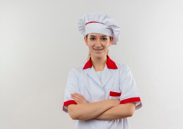 Smiling young pretty cook in chef uniform with dental braces standing with closed posture isolated on white space 