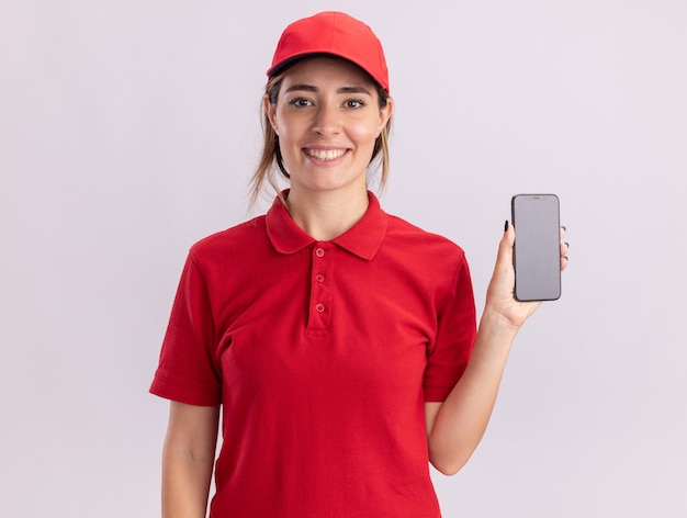 Smiling young pretty delivery girl in uniform holds phone on white