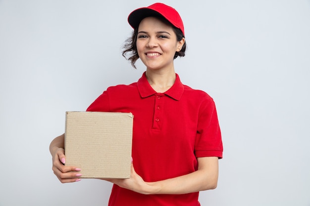 Smiling young pretty delivery woman holding cardboard box 