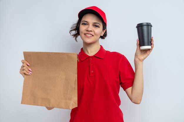 紙の食品包装とテイクアウトカップを保持している若いかわいい配達の女性の笑顔