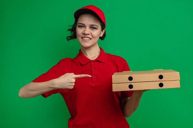 Smiling young pretty delivery woman holding and pointing at pizza boxes 