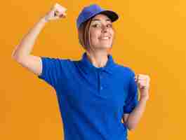 Free photo smiling young pretty delivery woman in uniform stands with raised fists isolated on orange wall