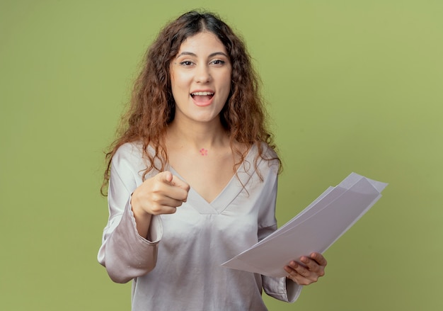 Sorridente giovane impiegato abbastanza femminile in possesso di documenti e mostrandoti gesto isolato su verde oliva