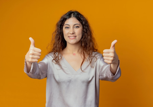 Smiling young pretty girl her thumbs up isolated on yellow wall