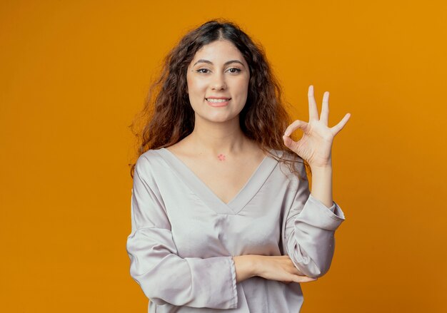 Smiling young pretty girl showing okey gesture isolated on yellow wall