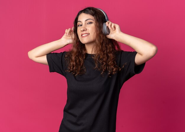 Smiling young pretty girl wearing and grabbing headphones 
