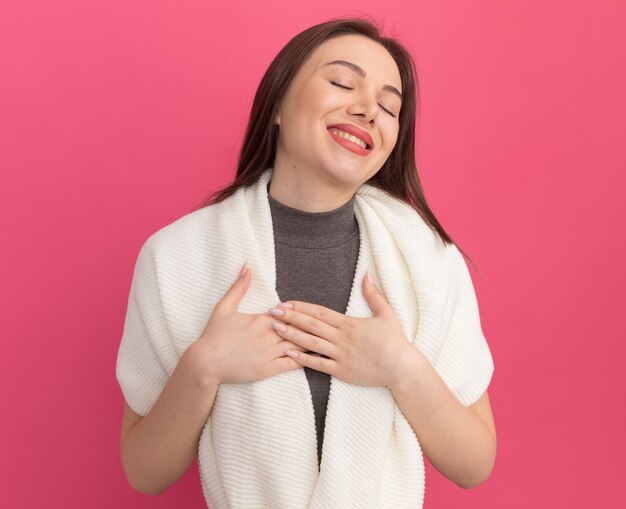 ピンクの壁に隔離された目を閉じてありがとうジェスチャーをしている笑顔の若いきれいな女性