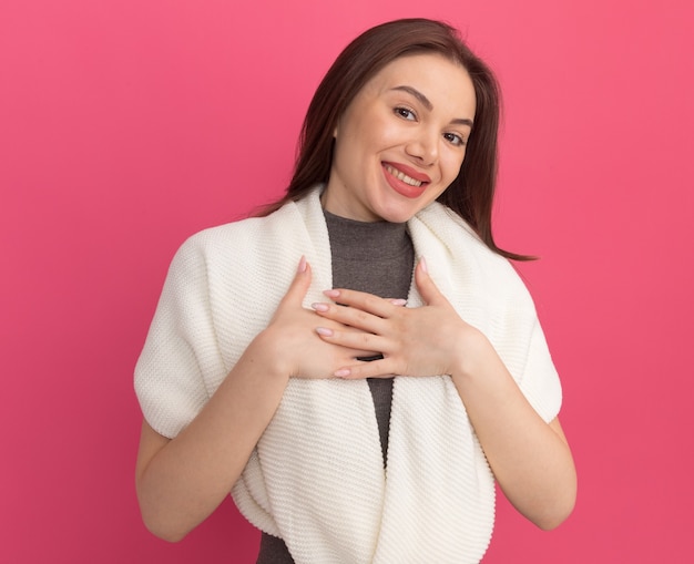 Sorridente giovane bella donna che tiene le mani sul petto facendo gesto di ringraziamento isolato sulla parete rosa