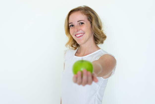Улыбается молодая красивая женщина, предлагая размытое зеленое яблоко