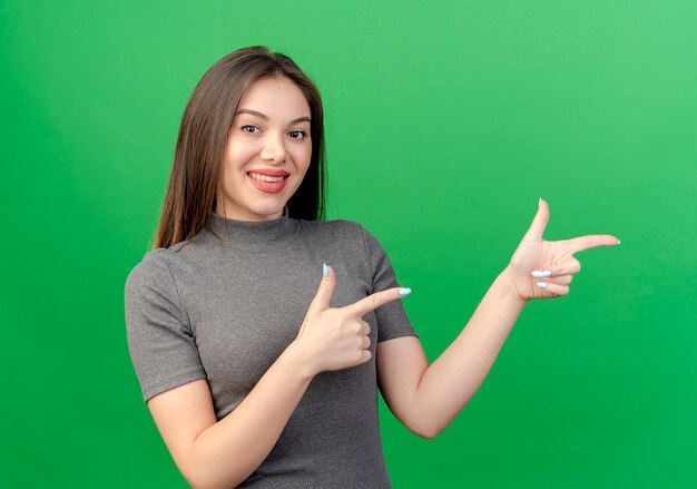 Smiling young pretty woman pointing at side isolated on green background