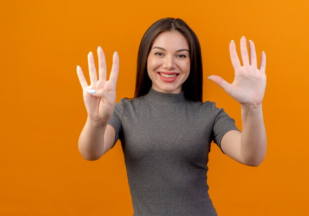 улыбающаяся молодая красивая женщина, показывающая четыре и пять с руками, изолированными на оранжевом